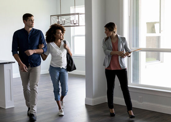 Realtor shows a couple a home. The realtor shows them the home's large living and kitchen area. The couple is expecting their first child.